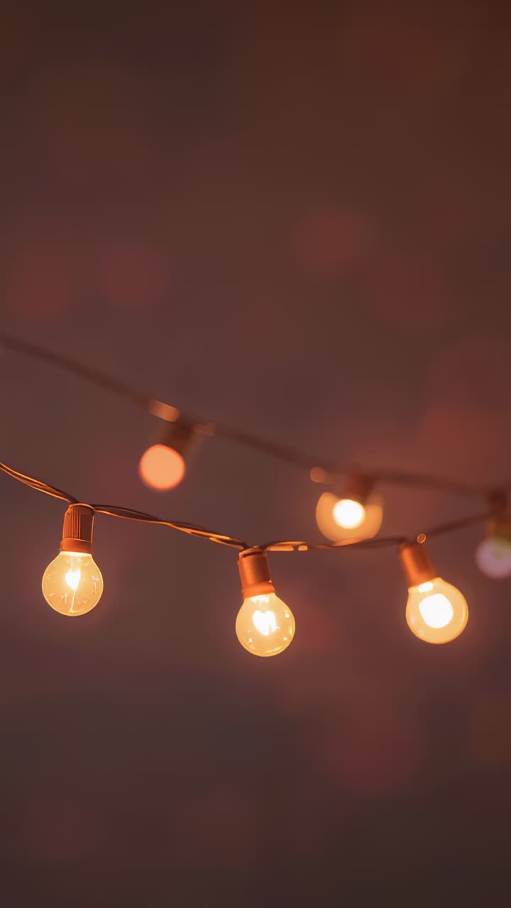 Vertical video: Shifting camera moving string of warm bulbs on porch to show filament glow, bokeh