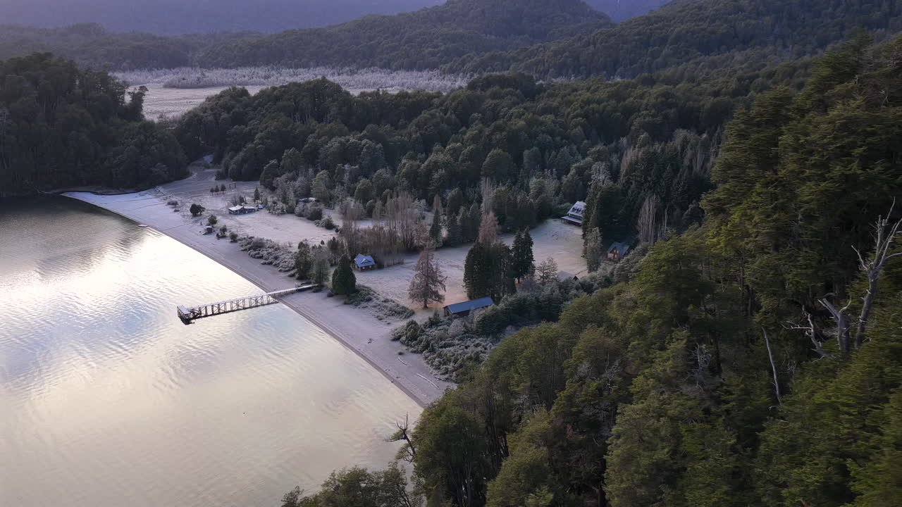 Bãi biển cát và bờ hồ có rừng cây của Lago Espejo gần Villa La Angostura, tỉnh Neuquén, Patagonia, Argentina, với bến tàu và các căn nhà nhỏ dọc theo mặt nước hồ yên ả dưới chân dãy Andes. Máy bay không người lái quay quét và hé lộ cảnh quan.