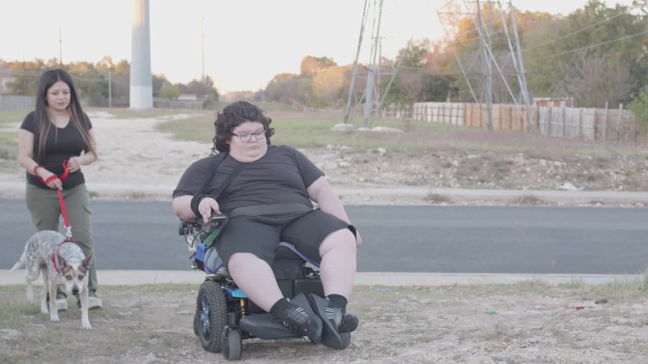 Muscular Dystrophy adolecsent in wheelchair dog walking with mom in field
