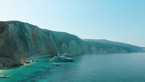 luxury yachts moored in a beautiful bay with stunning cliffs and clear turquoise water.