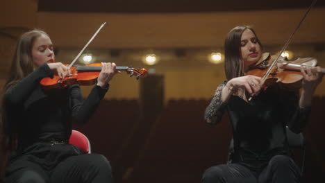 female violinists are playing music in orchestra sitting on scene of philharmonic hall