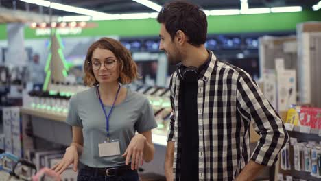 en la tienda de electrónica - una consultora positiva da consejos profesionales a un joven. necesita la opinión de un experto. la tienda es moderna, luminosa y tiene todos los dispositivos nuevos. conversación. cámara lenta