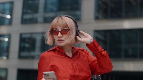 stylish woman listening to music and checking phone in city