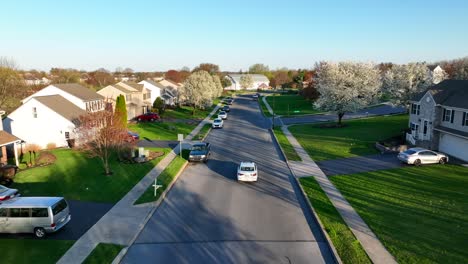 Weißes-Auto-Fährt-Langsam-In-Ruhiger-Amerikanischer-Wohngegend,-Drohnenverfolgungsauto-Aus-Der-Luft,-Wohngebiet-In-Den-USA,-Grüner,-Warmer-Frühling