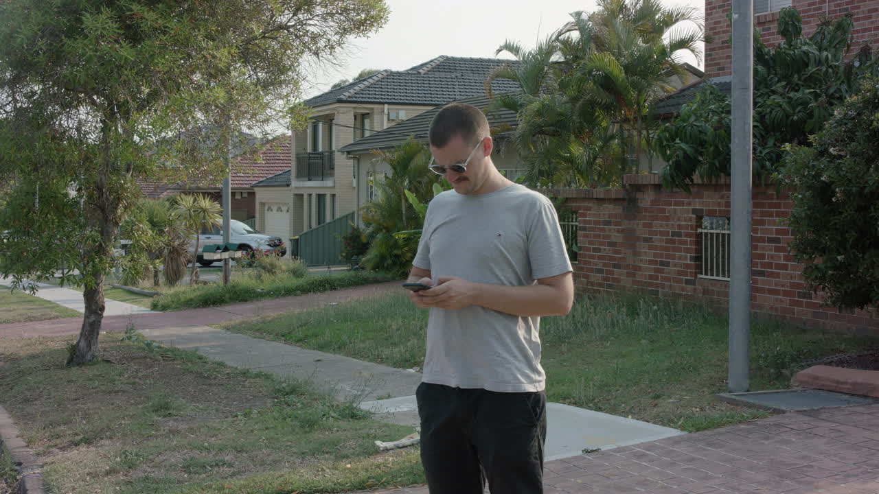 Plano medio estático de un joven estresado enviando mensajes de texto en una calle ventosa por la tarde.