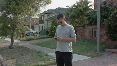 Toma-Estática-Media-De-Un-Joven-Estresado-Enviando-Mensajes-De-Texto-Por-Una-Calle-Ventosa-Por-La-Tarde