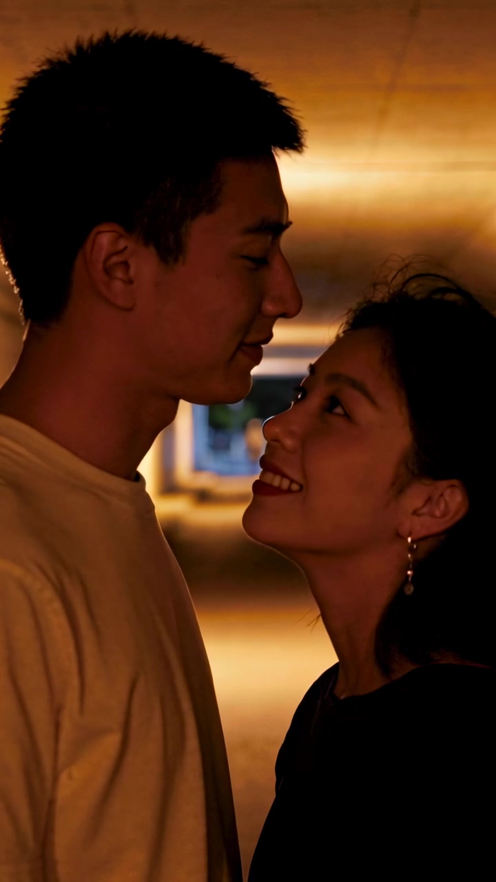 Vertical video: Leaning couple closing on chin lift sharing love under amber lights with earrings