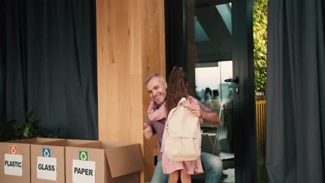 A-Happy-little-brunette-girl-in-a-pink-skirt-with-a-white-backpack-runs-to-her-dad-after-lessons-in-a-club-for-preparing-children-for-school