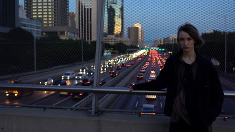 woman on a bridge overlooking a busy city highway at dusk