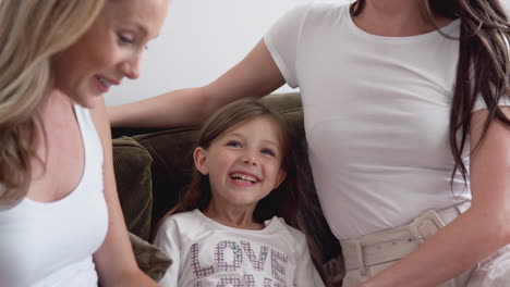 same sex female couple reading book with daughter at home together