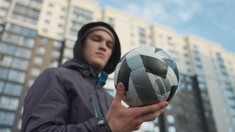 man spinning soccer ball on palm with focused expression, demonstrating dexterity and balance, blurred background highlights urban high-rise buildings