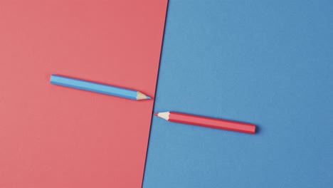 Overhead-view-of-blue-and-red-crayons-arranged-on-red-and-blue-background,-in-slow-motion