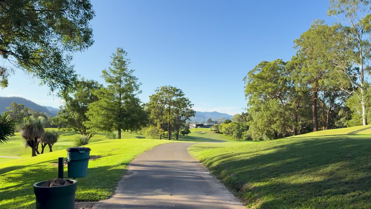 A peaceful walk on a sunlit golf course path, surrounded by lush greenery and clear blue skies