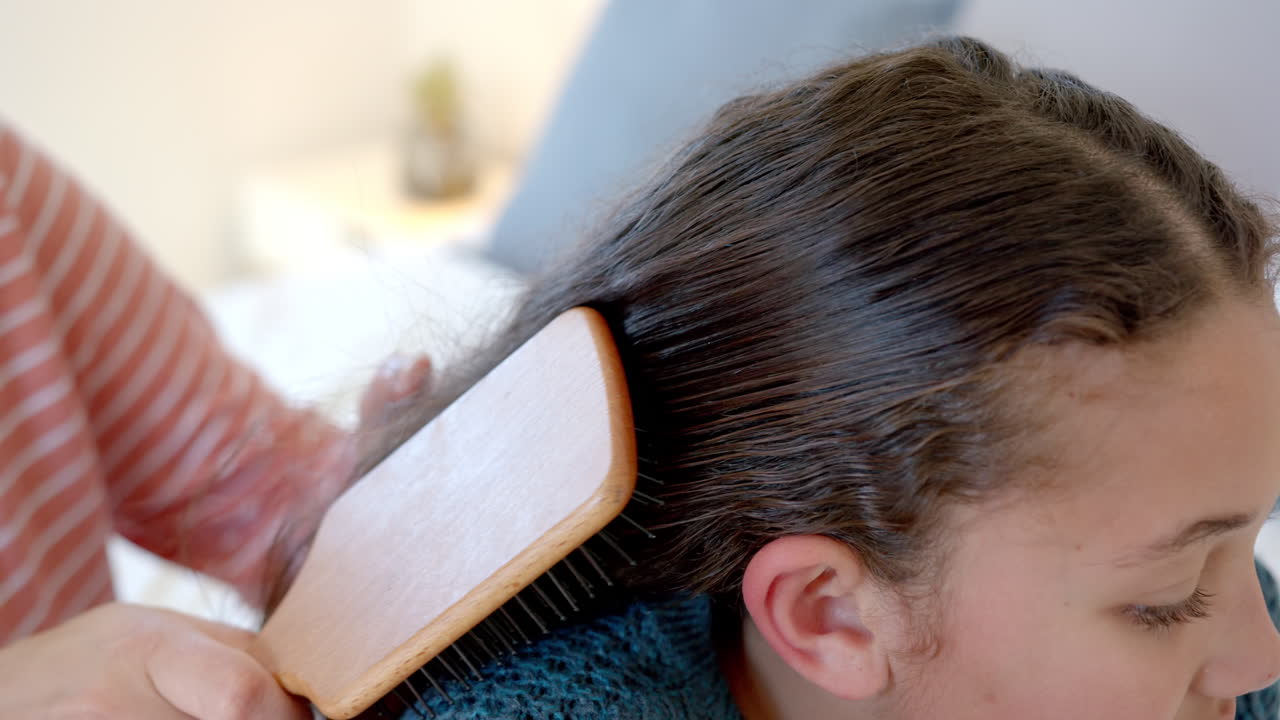 행복 한 혼혈 어머니 가 빛 이 있는 침실 에서 딸 의 머리 를 고 있다