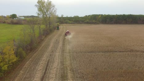 Drone-fly-above-trees-revealing-farm-land-with-machines-working-on-harvesting-season