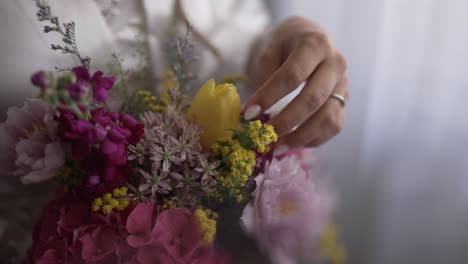 bride’s hand gently touches a vibrant floral bouquet with wedding ring visible