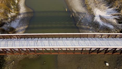 snow covered foot bridge in a park over a river - aerial pull back tilt up to reveal the magical landscape