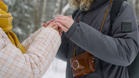 Close-Up-View-Of-A-Man-And-A-Woman-Warming-Their-Hands-In-The-Snowy-Forest