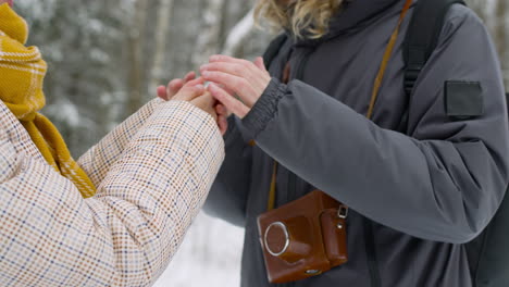 close up view of a man and a woman warming their hands in the snowy forest