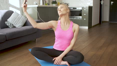 Junge-Attraktive-Sportliche-Frau-Sitzt-Auf-Yogamatte-Und-Macht-Selfie-Mit-Ihrem-Handy