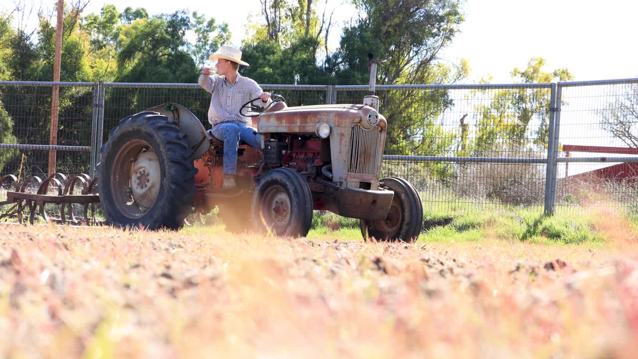 vaquero mirando por encima de la tierra en el tractor desgarrando el pasto
