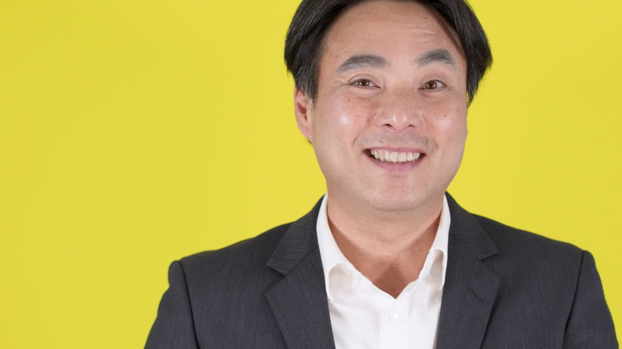 Businessman in formal suit forms heart gesture with hands, smiling, under bright studio lighting
