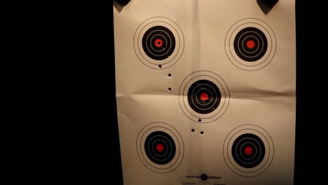 a man looks at the camera and then fires a hand gun at a target at an indoor shooting range 1