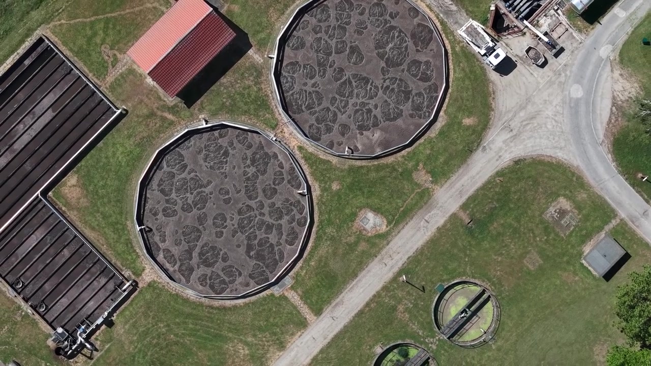 Aerial perspective of industrial water treatment tanks where liquid is actively processed, showing a complex network of pipes and machinery.