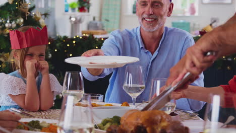 Portrait-Of-Multi-Generation-Family-Celebrating-Christmas-At-Home-Wearing-Paper-Hats-Eating-Meal