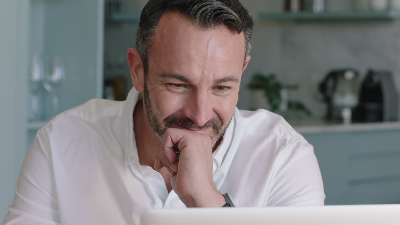 attractive man using laptop working at home browsing online reading social media messages on computer drinking coffee enjoying digital communication