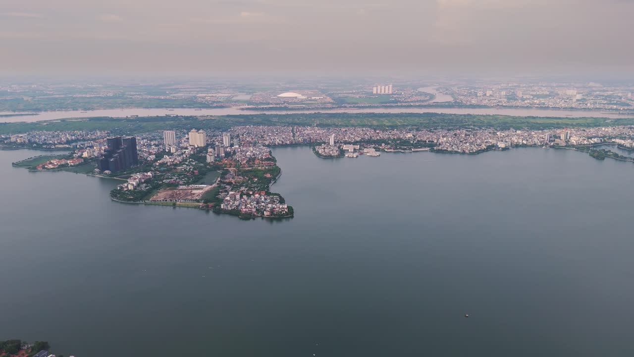 Aerial footage of Hanoi's West Lake (Tay Ho) during the day. The shot captures the vast lake surrounded by a mix of modern high-rises and residential areas. UHD
