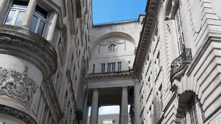 Strada stretta a Londra con edifici storici collegati da un arco sorretto da colonne. Veduta dal basso verso l'alto che mostra la facciata dettagliata e gli elementi architettonici