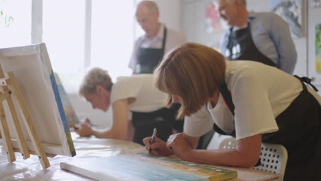 happy group of senior people paint pictures together in class.