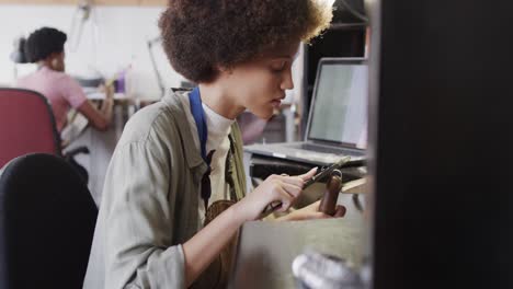 busy biracial female worker with laptop shaping jewellery in studio in slow motion