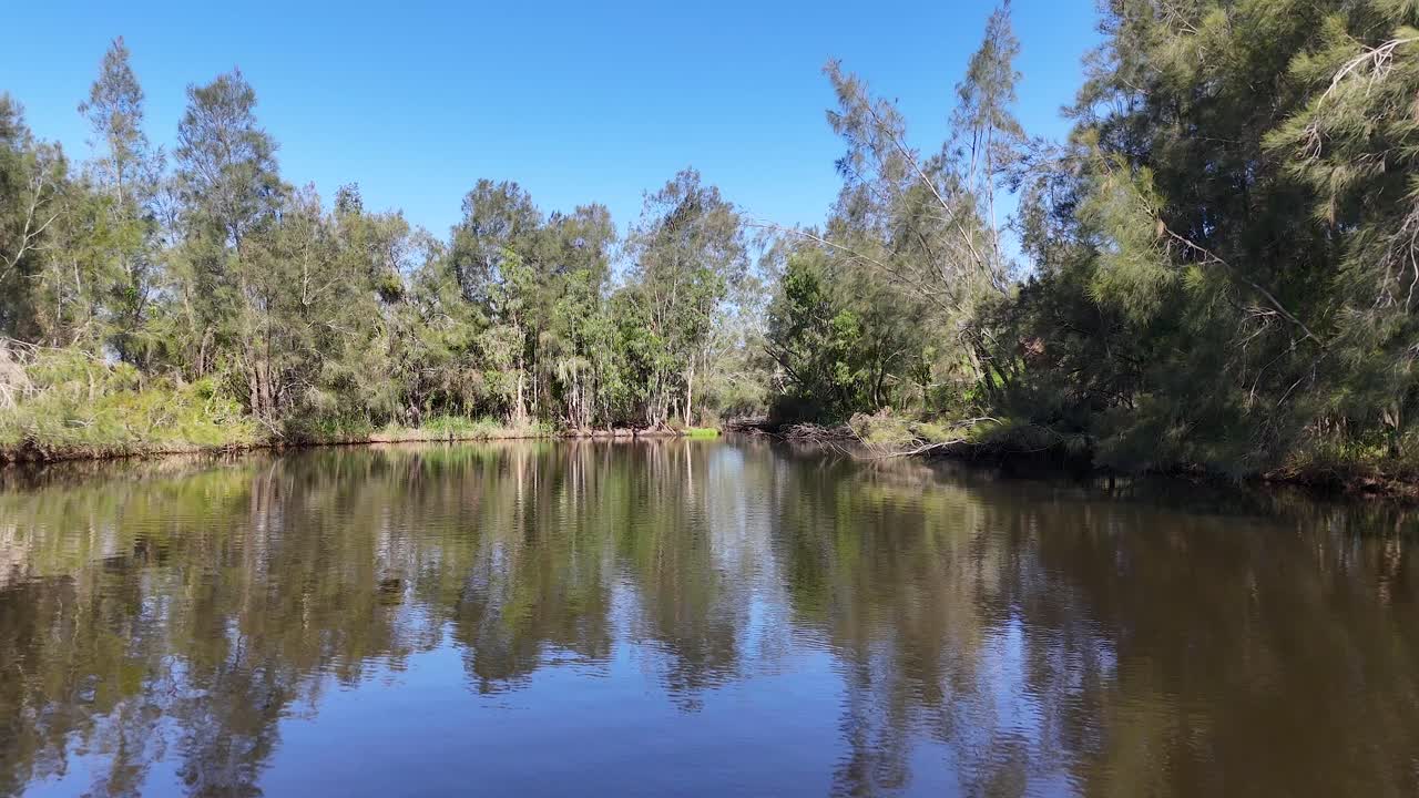 Slow pan across tranquil Australian wetland lake, trees reflecting on still water under clear daylight