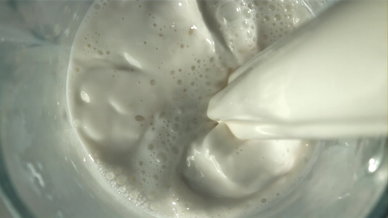 Cámara lenta: Vertiendo leche blanca en un vaso con salpicaduras.
