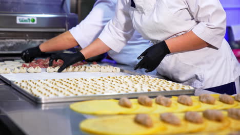 workers at food factory make dumplings with minced meat. freshly-made half-stuff products are laid on the trays on the table.