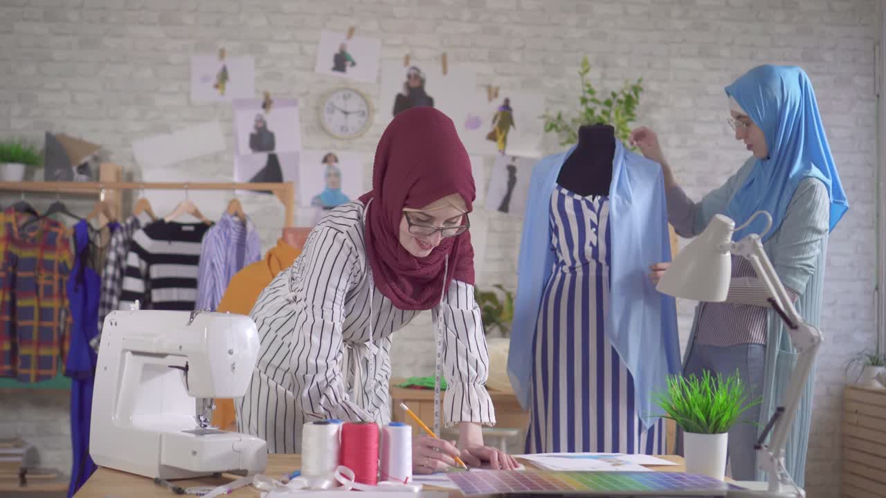 Desainer mode wanita Muslim muda berkerudung sedang bekerja di studio modern.