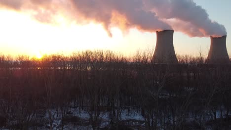 dolly up aerial drone shot of nuclear power plant cooling towers at sunrise sunset with steam and smoke bright sun winter