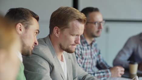 tracking shot of two middle aged men whispering in meeting sharing secrets. group of business people sitting on desk