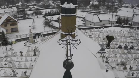 drone view of a snow covered village in the valley below a mountain range, focusing on large church and cemetery