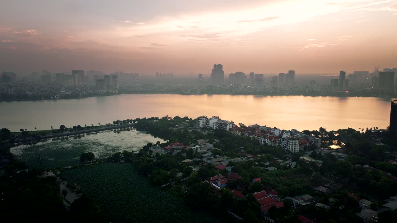 Drone establishing trucking pan of sunset over Hanoi’s Ho Tay Lake, with reflections on the water and a city skyline under golden skies