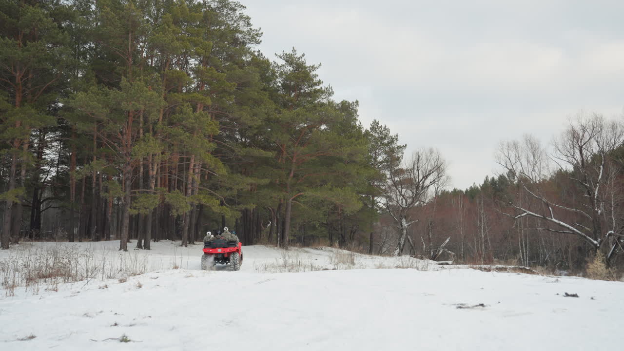 Quad rosso sfreccia attraverso un campo innevato, il pilota spinge l'acceleratore mentre l'ATV solleva la neve in aria, sfondo panoramico di pini, cielo coperto, corsa estrema e ad alta energia, movimento dinamico e inquadratura ampia.