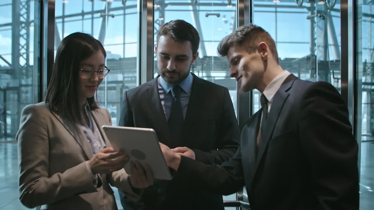 Businesswoman And Two Businessmen In A Elevator Talking And Looking A Tablet 1