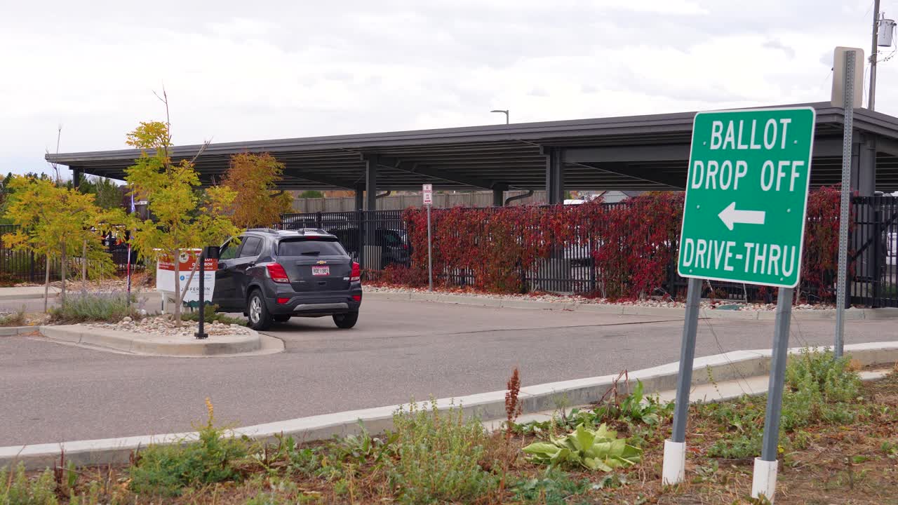 A woman drives to a ballot drop box and casts her mail-in vote from the car window, symbolizing empowerment, equal rights, civic duty, democracy, election integrity, and accessible participation
