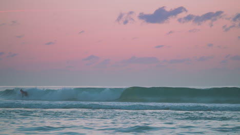 un surfista atrapando una ola con una hermosa puesta de sol rosa y azul detrás de él