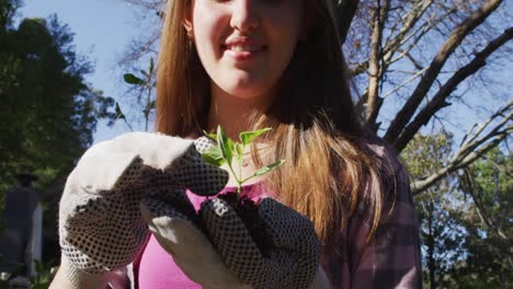 Lächelndes-Kaukasisches-Teenager-Mädchen,-Das-Mit-Handschuhen-Im-Garten-Arbeitet-Und-Pflanzen-Inspiziert