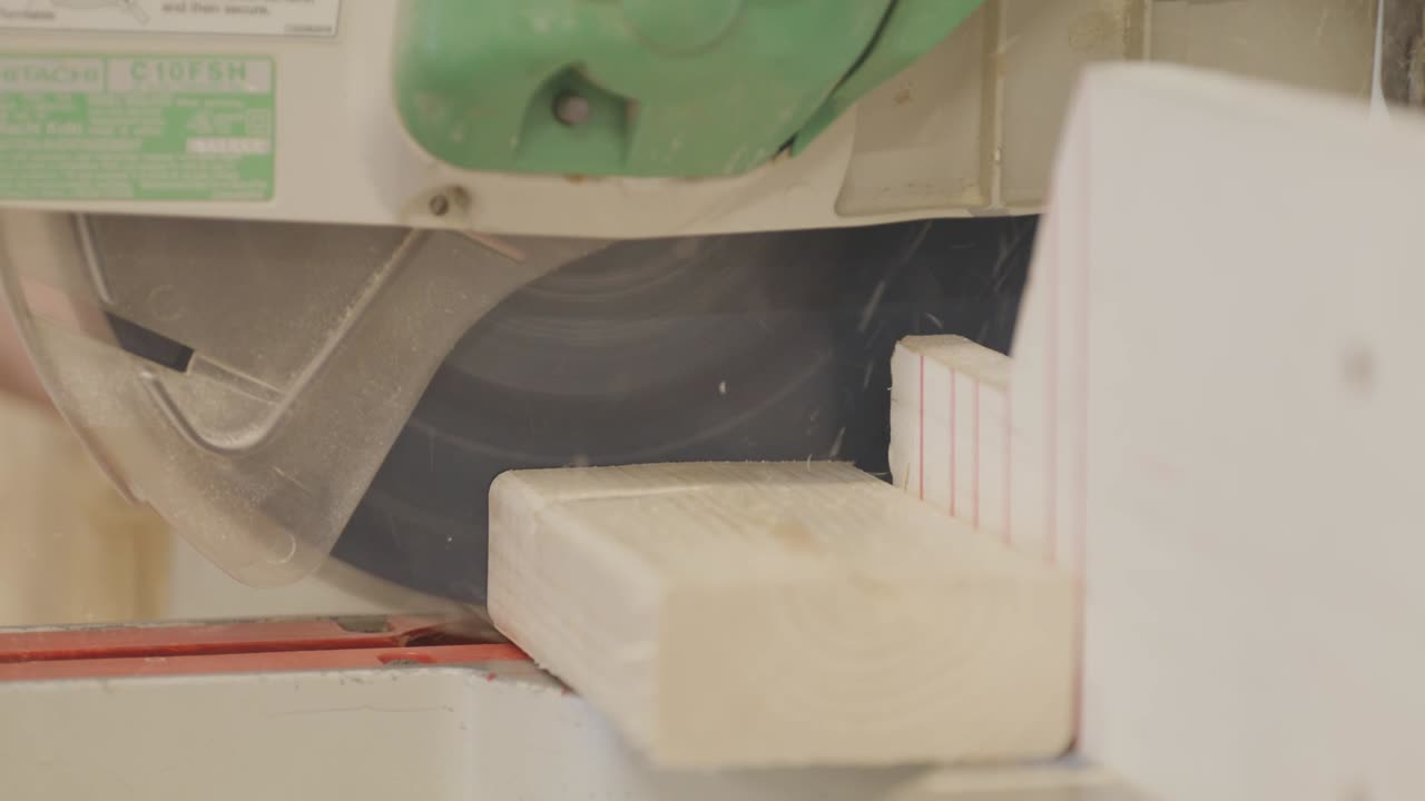 Man using miter saw cutting a piece of wood with video close up in slow motion.