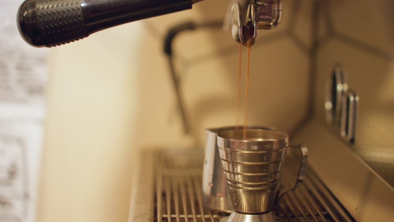 Versamento costante in un misurino. Preparazione casalinga concentrata con pressione controllata e bilancia trasparente. Scena minimalista di espresso versato con precisione in una tazza di metallo che mostra controllo attento e concentrazione