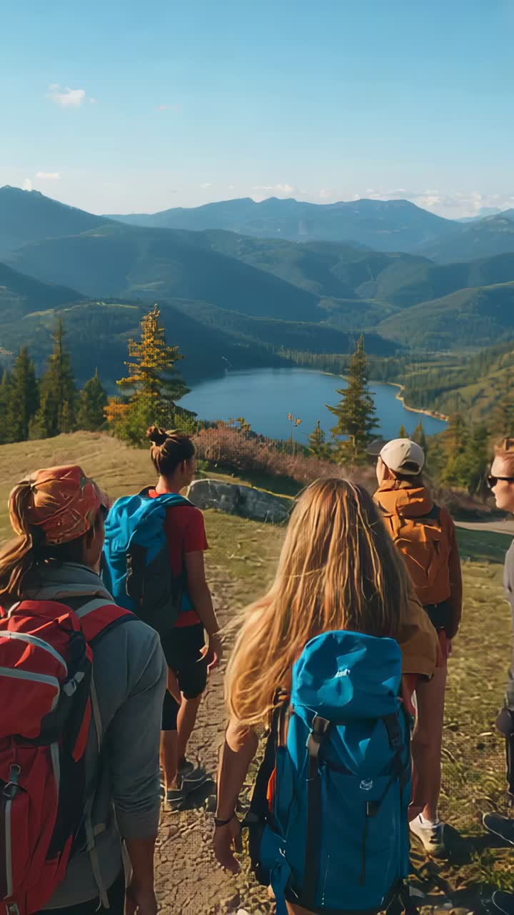 Vertical video: Camera starting behind 5 hikers walking ridge toward lake in gear with blue pack